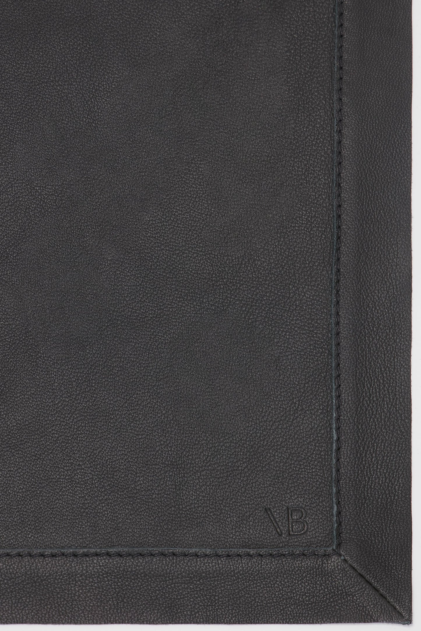 Close-up view of a classic black, supple leather surface with visible stitching along the edge and the initials "V B" embossed in the corner, featuring the Leather Scarf In Black from Victoria Beckham.