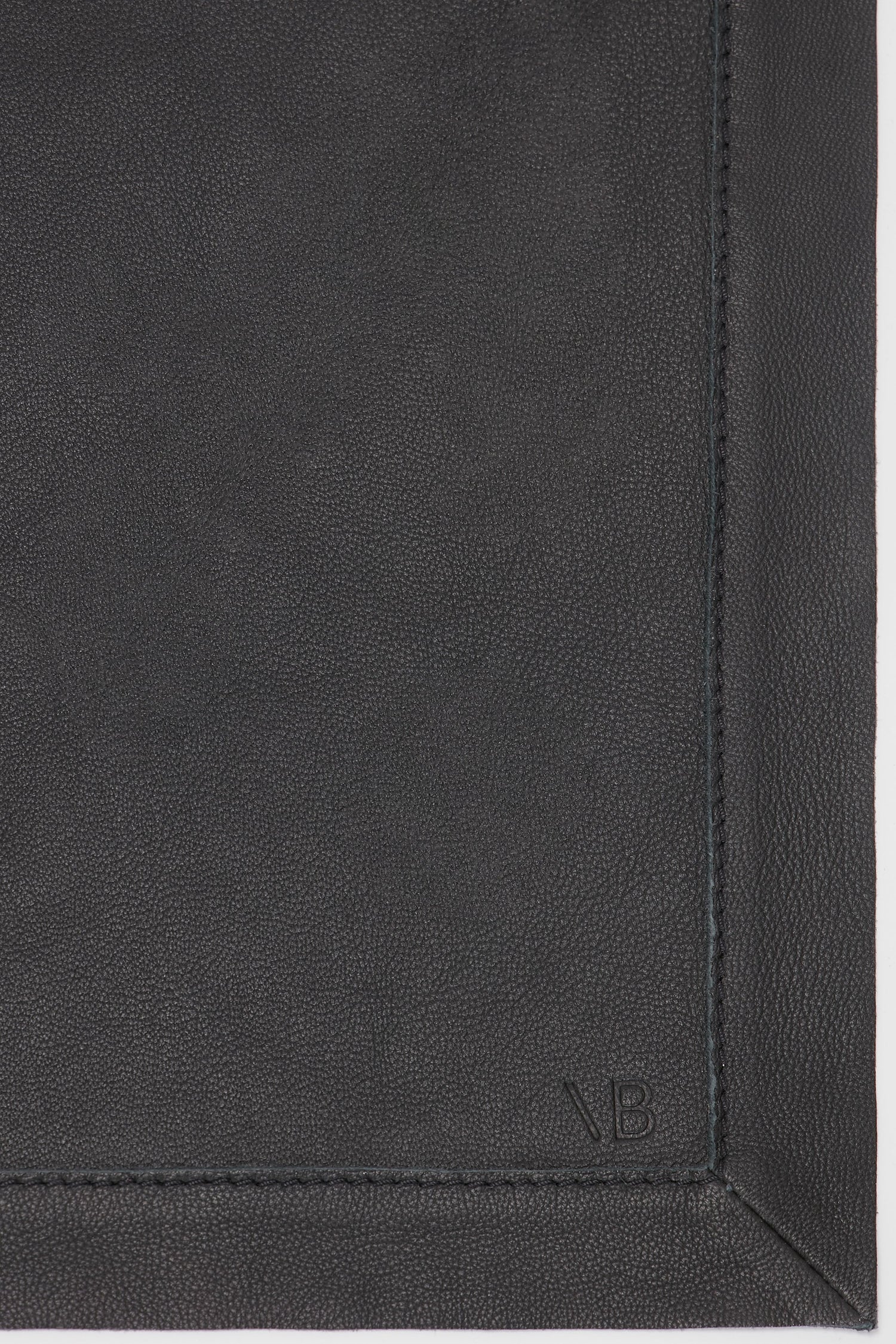 Close-up view of a classic black, supple leather surface with visible stitching along the edge and the initials "V B" embossed in the corner, featuring the Leather Scarf In Black from Victoria Beckham.