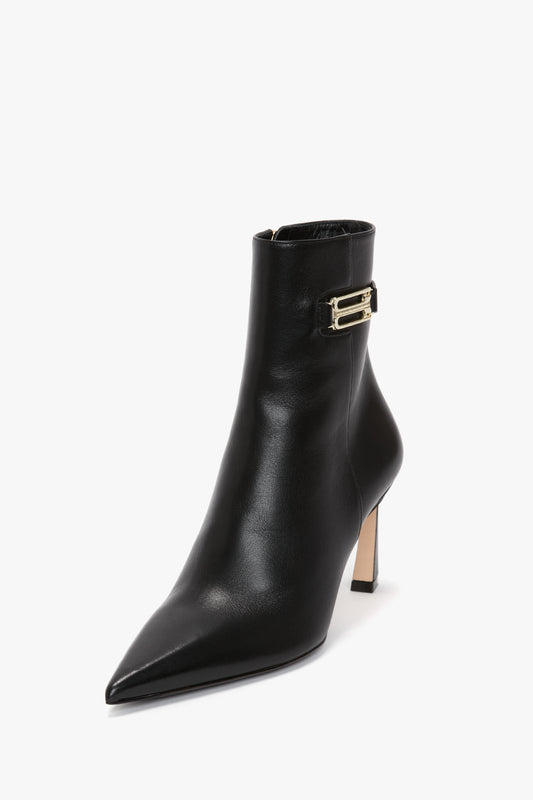 A Pointed Toe Half Boot In Black Soft Calf Leather by Victoria Beckham, with a pointed toe and a sculptural heel, featuring a gold decorative buckle near the top.