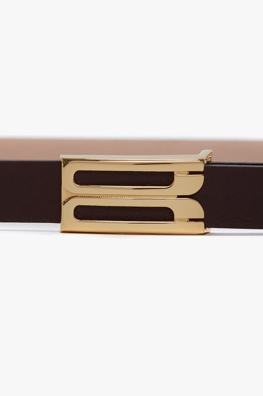 A close-up image of a dark brown Exclusive Micro Frame Belt In Burgundy Leather, crafted from smooth calf leather and featuring gold hardware with a rectangular buckle that has two parallel slots by Victoria Beckham.