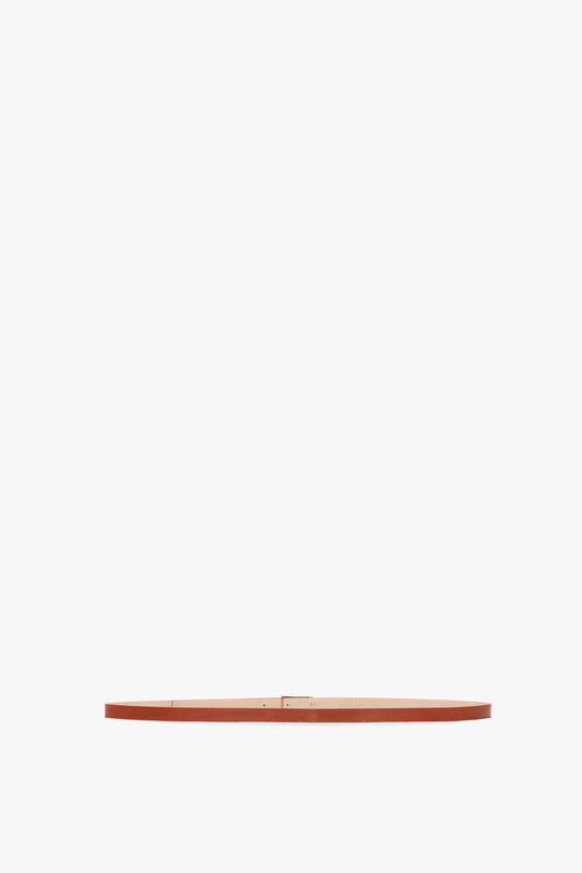 A thin, flat, circular orange object is centered against a white background, resembling the elegance of Victoria Beckham's Exclusive Micro Frame Belt In Tan Leather with gold hardware.
