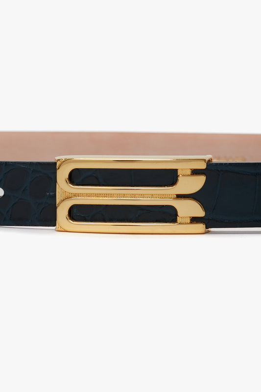 A close-up of a Victoria Beckham Frame Belt In Midnight Blue Croc Embossed Calf Leather with a gold double-prong buckle and a black croc-embossed leather strap with a textured pattern.