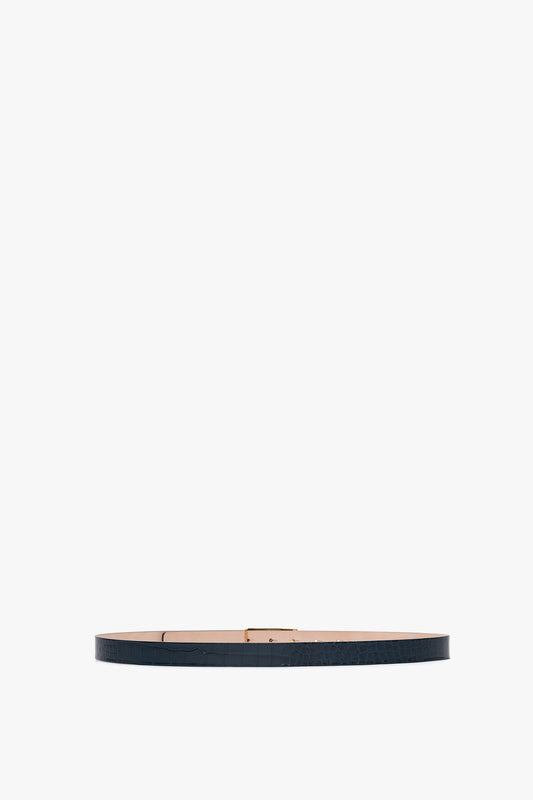 A thin, dark-colored, croc-embossed leather belt with a simple buckle, placed against a white background has been replaced with the Frame Belt In Midnight Blue Croc Embossed Calf Leather by Victoria Beckham.