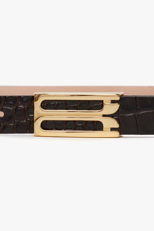 A close-up of a Victoria Beckham Frame Belt In Espresso Croc Embossed Calf Leather with gold hardware detailing the buckle.