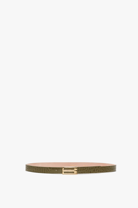 A slim, green croc-embossed calf leather Exclusive Frame Belt In Khaki Croc Embossed Calf Leather with a textured pattern and gold hardware in the form of a rectangular buckle, displayed against a white background by Victoria Beckham.