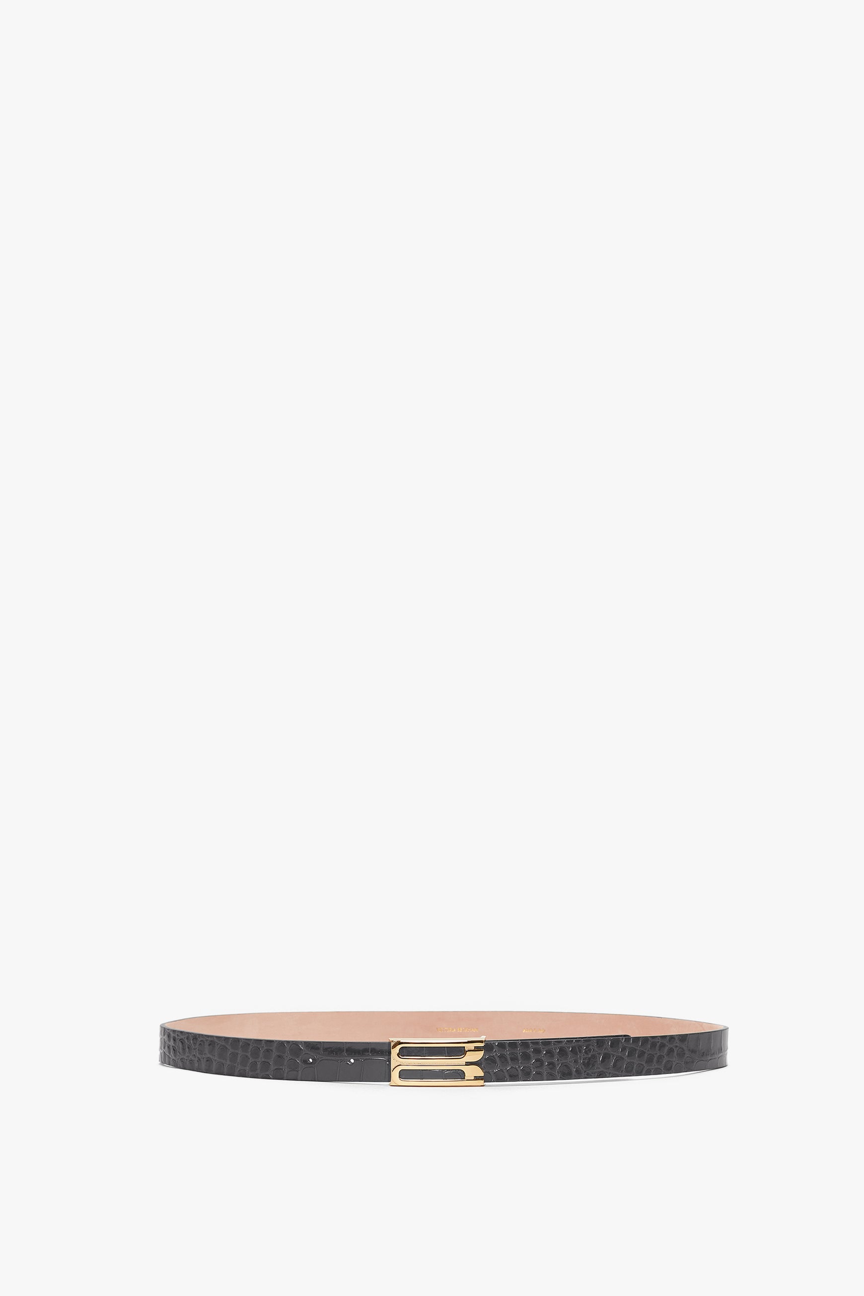 A thin, slate grey Frame Belt In Slate Grey Croc Embossed Calf Leather crafted from croc-embossed calf leather features a gold rectangular buckle on a white background by Victoria Beckham.
