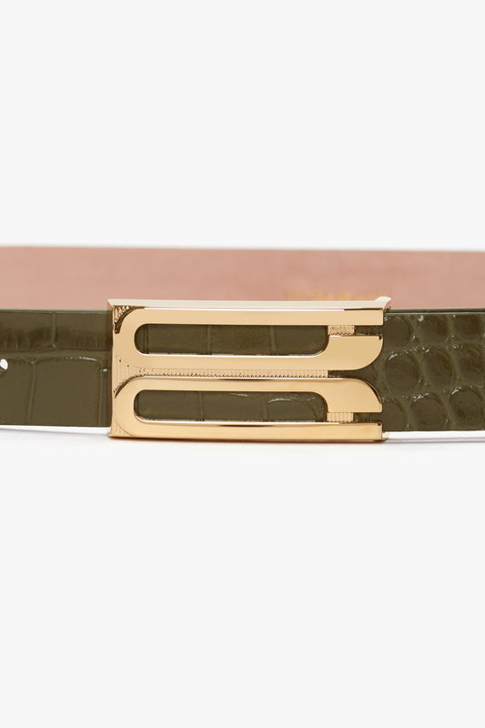 Close-up of the Exclusive Frame Belt In Khaki Croc Embossed Calf Leather by Victoria Beckham with a textured surface and a gold, square-shaped buckle featuring two vertical cutouts.