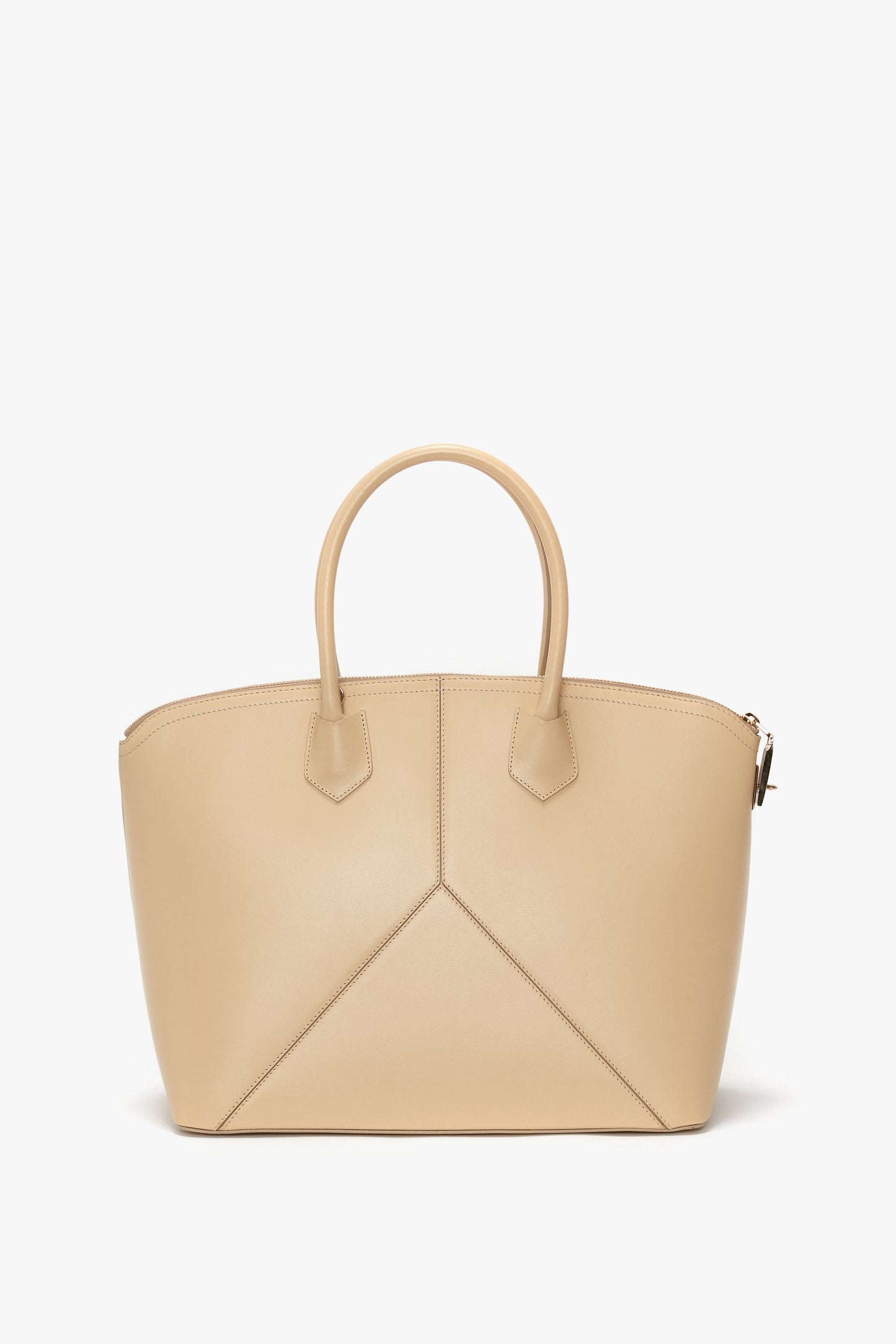 The Victoria Beckham Victoria Bag In Sesame Leather is a beige leather handbag with an arch-shaped top and two handles. It showcases stitched geometric designs on the front and a zipper closure on top, complemented by leather panels. The background is plain white.