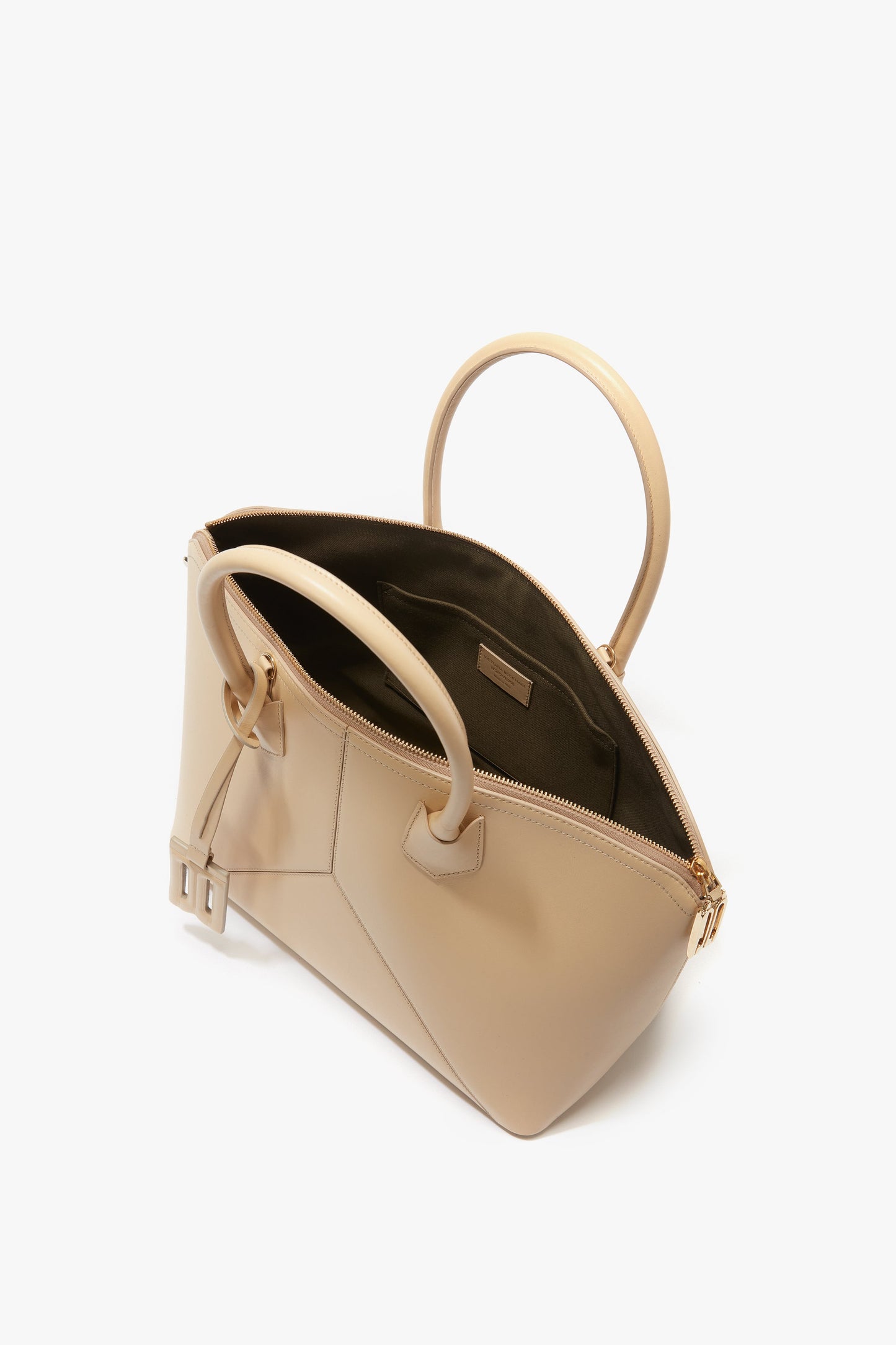 The Victoria Beckham Victoria Bag In Sesame Leather boasts sophisticated leather panels, two handles, and an open zipper. Its spacious interior includes a small inner compartment and elegant side buckle details. Plus, it features an adjustable strap for added versatility.