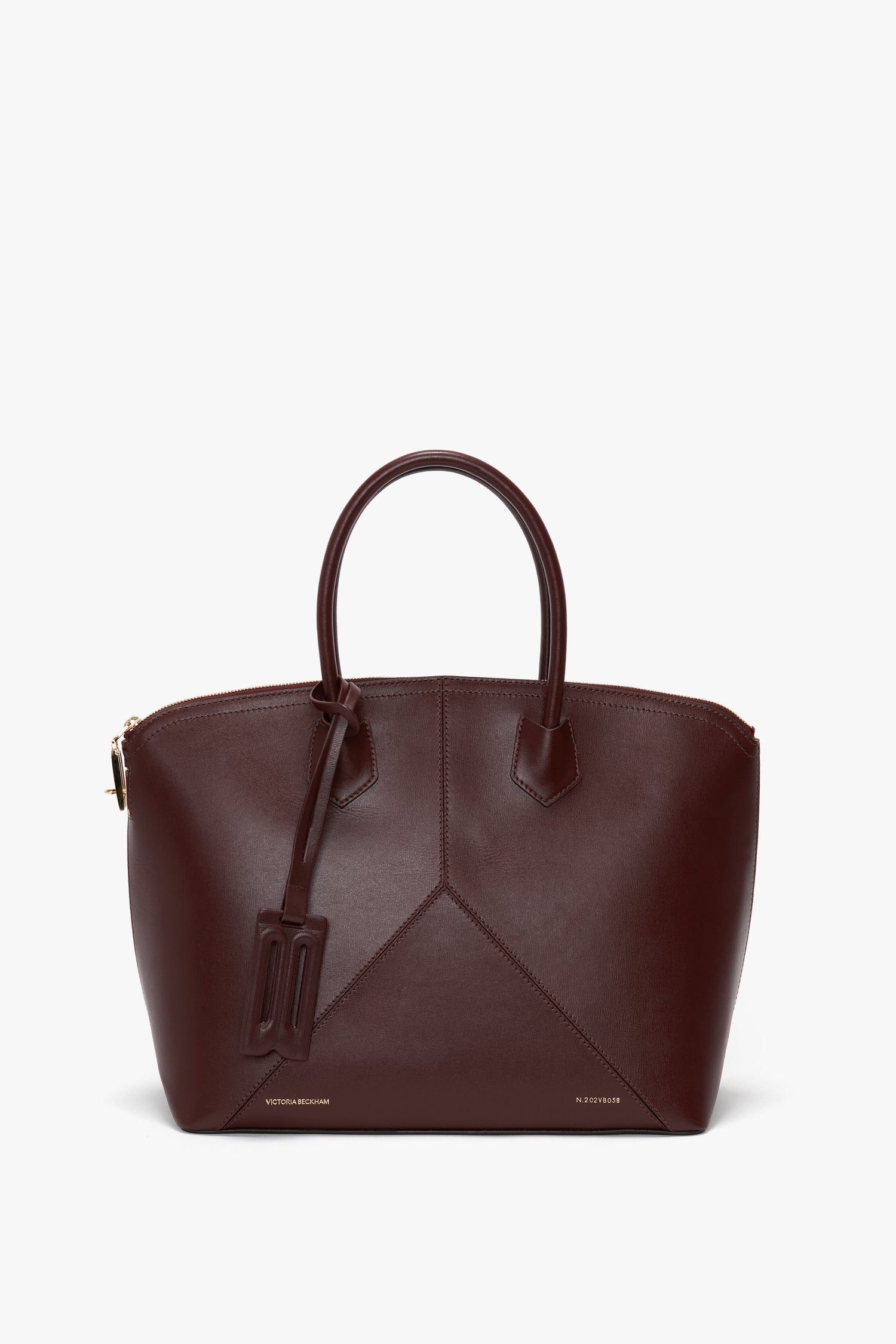 A burgundy leather Victoria Bag In Burgundy Leather by Victoria Beckham with a structured design, two top handles, a padlock closure, and a hanging charm accessory.