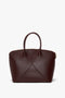 A **Victoria Bag In Burgundy Leather** by **Victoria Beckham** with a structured design, featuring top handles and a padlock closure, set against a white background.