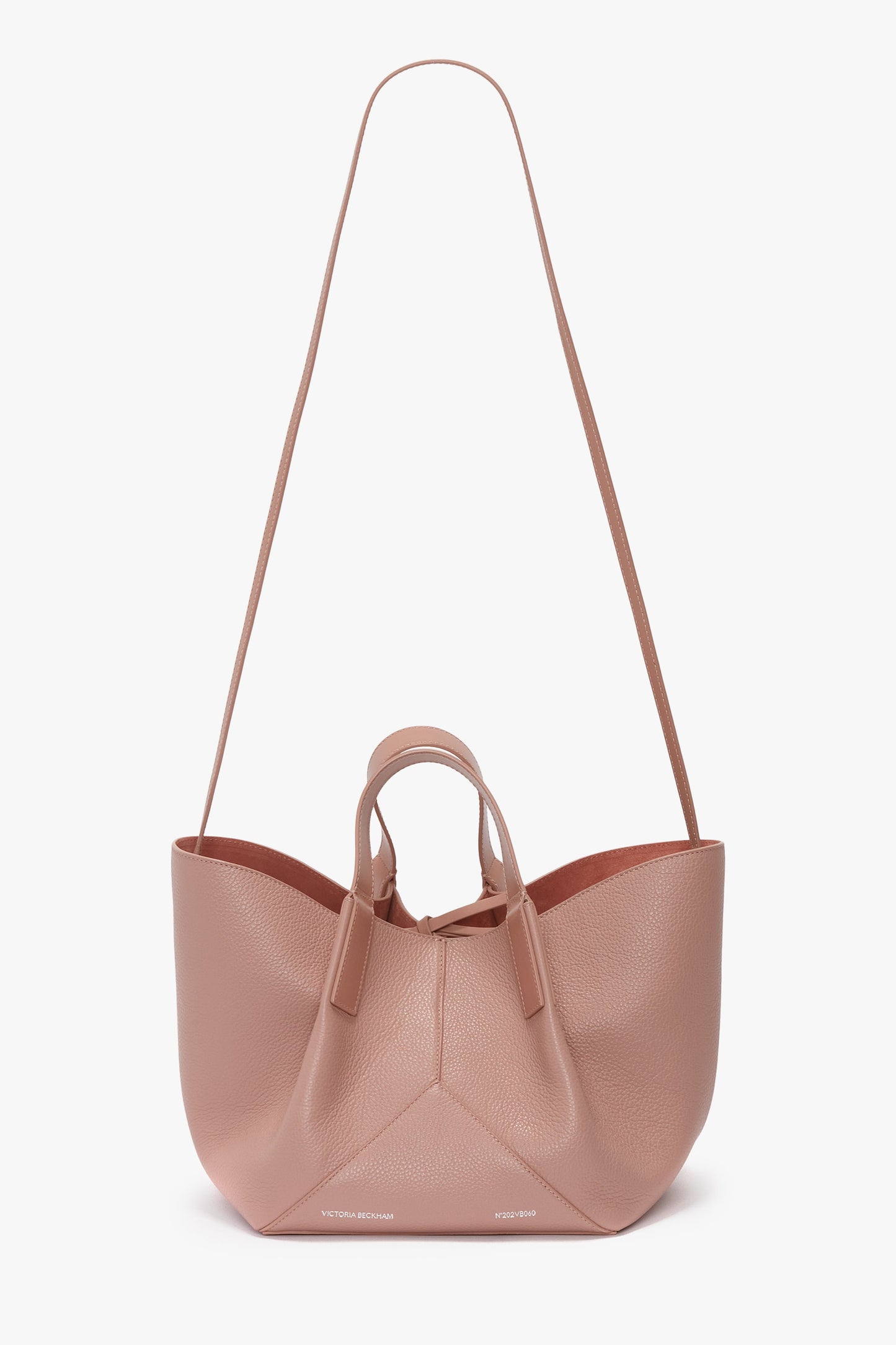 The W11 Mini Tote Bag In Marshmallow Leather by Victoria Beckham, crafted from light pink textured calf leather, features two short handles and a long shoulder strap, perfect as a crossbody bag. Displayed against a plain white background, this stylish accessory is versatile and chic.