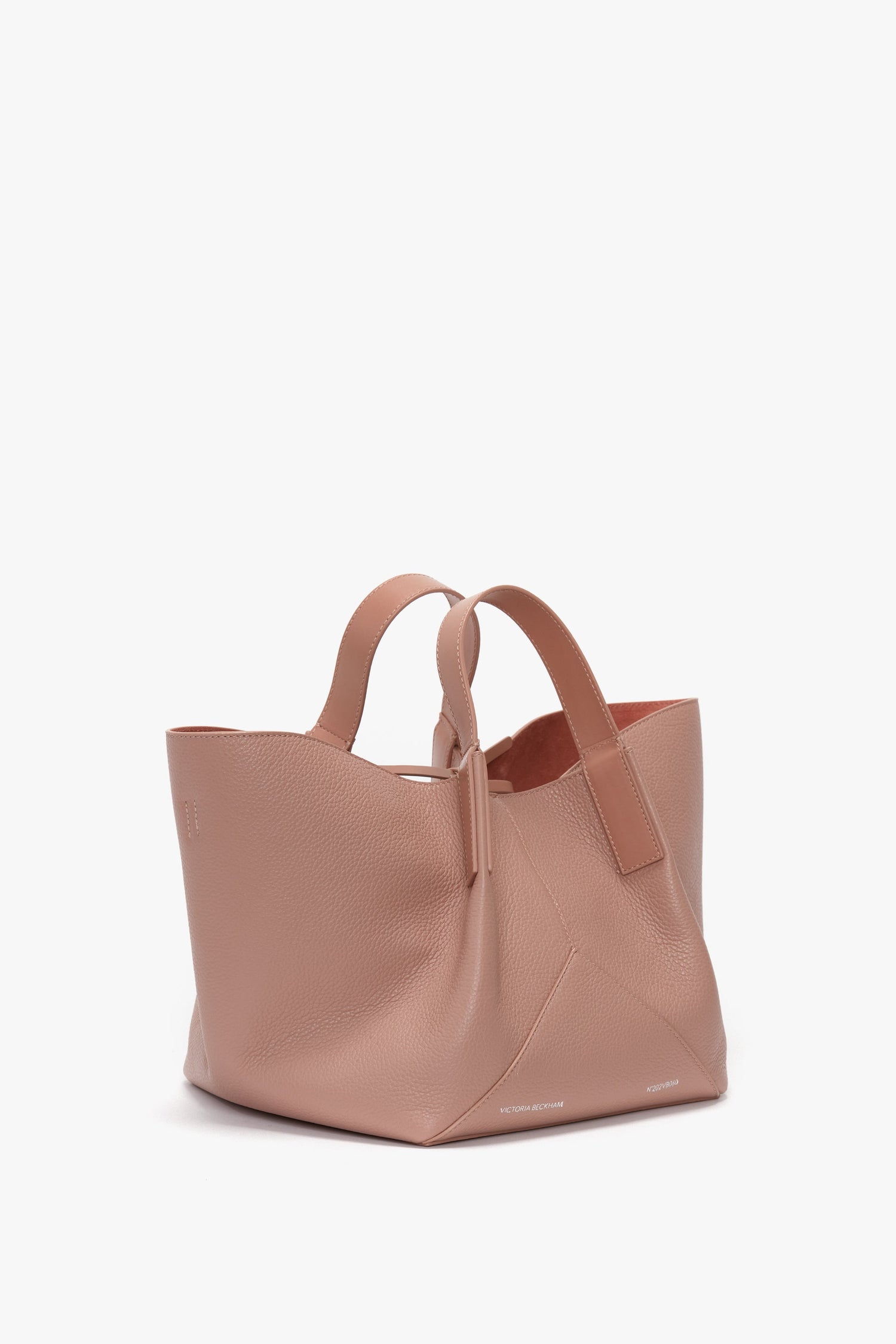Image of a W11 Mini Tote Bag In Marshmallow Leather by Victoria Beckham in pink calf leather, featuring two handles, a geometric design, and a soft texture. The bag appears to be empty and is displayed against a white background.