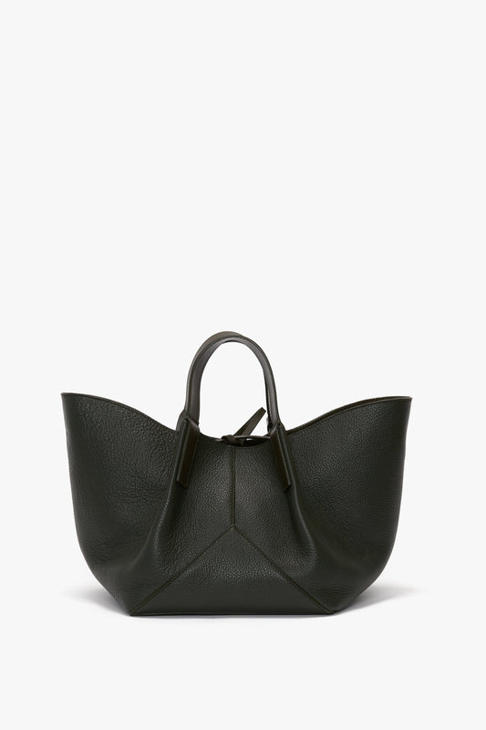 A dark green W11 Mini Tote Bag In Loden Leather handbag crafted from calf leather, featuring short handles and a unique, curved design by Victoria Beckham.