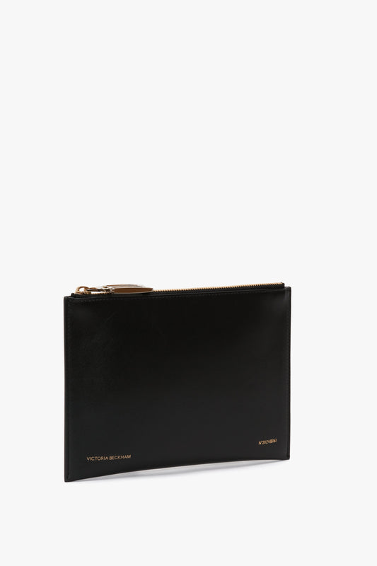A B Frame Pochette Bag In Black Leather with gold-tone hardware and the name "Victoria Beckham" embossed in gold at the bottom left corner. This modern accessory boasts a compact design perfect for stylish storage on the go.