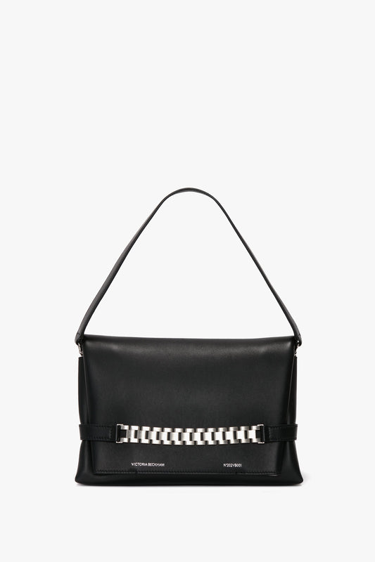 A black leather Chain Pouch Bag with Brushed Silver Chain In Black Leather by Victoria Beckham with a single top handle, featuring a rectangular shape and a distinctive brushed silver chain detail on the front. Includes a convenient detachable strap for versatile carrying options.
