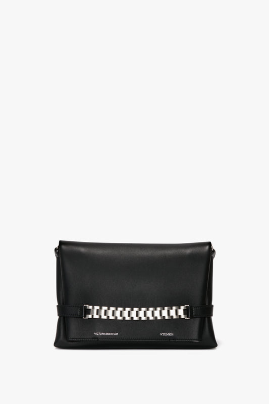 A sleek black rectangular handbag featuring a brushed silver chain detail on the front and discreet text at the bottom, complete with a detachable strap for versatile wear. This is the Victoria Beckham Chain Pouch Bag with Brushed Silver Chain In Black Leather.