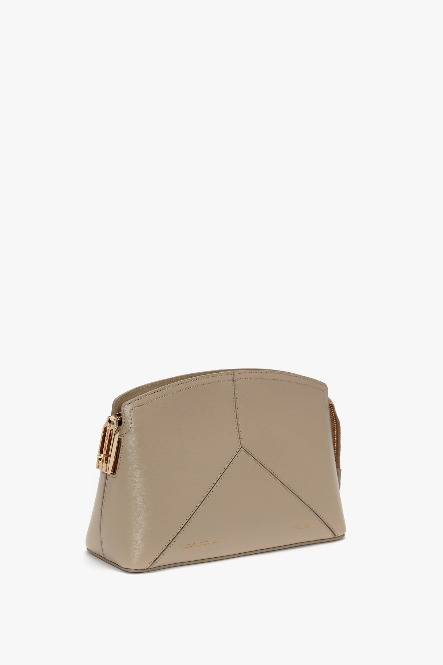 A **Victoria Crossbody Bag In Taupe Leather** by **Victoria Beckham**, featuring gold hardware, a structured, geometric design, and visible stitching along the front. The background is plain white, echoing the refined elegance often seen in Victoria Beckham's collections.