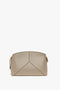 A **Victoria Beckham Victoria Crossbody Bag In Taupe Leather** with a structured geometric design and minimal stitching, featuring a gold zipper on the right side, reminiscent of Victoria Beckham's chic style.