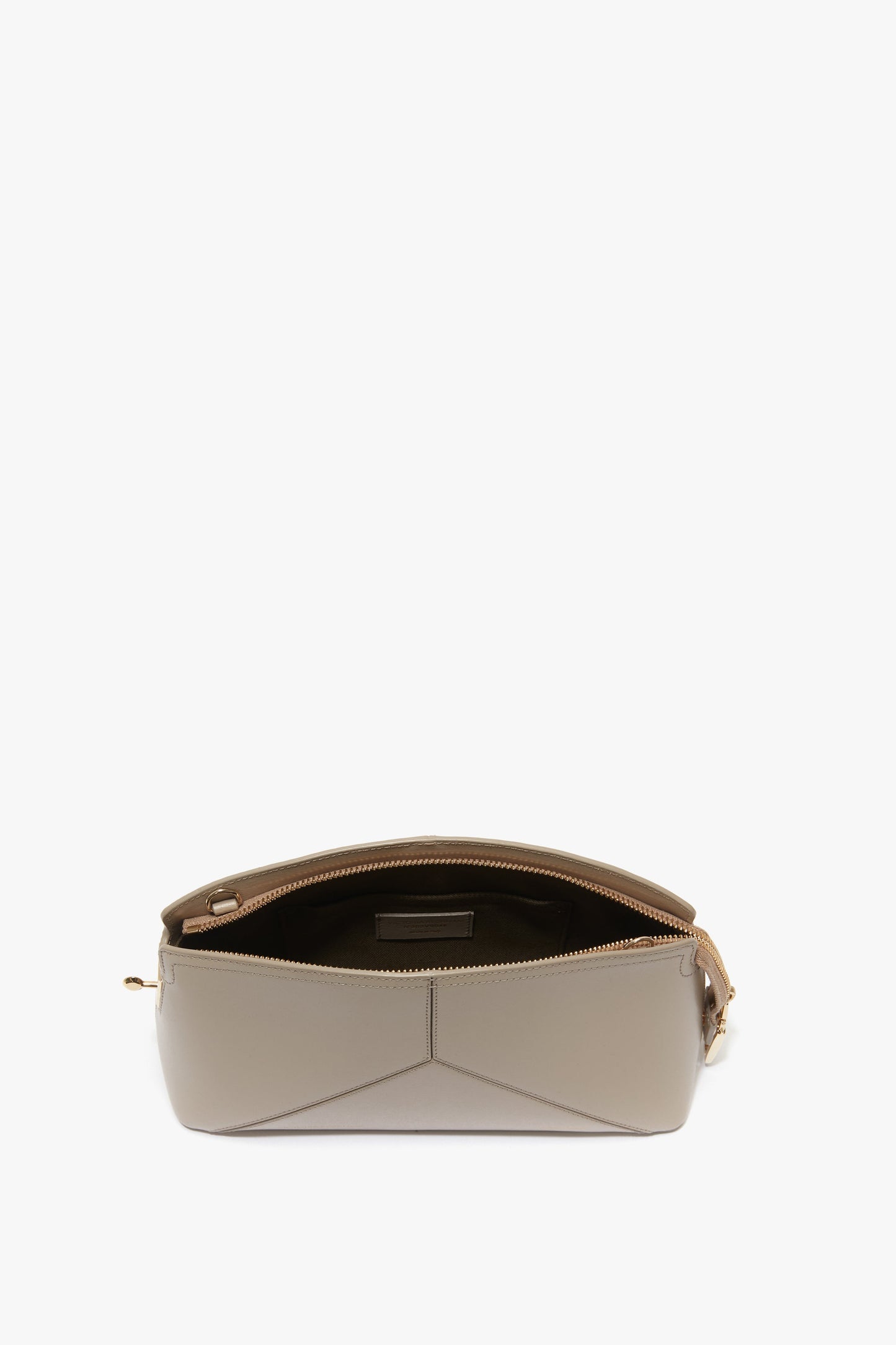 A Victoria Crossbody Bag In Taupe Leather by Victoria Beckham, with a structured geometric design, showcases an open zipper revealing an empty beige interior.