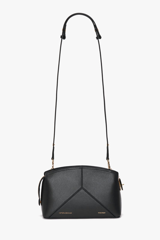 A small, black calf leather Victoria Beckham Victoria Crossbody In Black Leather with a long adjustable strap, minimalist gold hardware, and geometric stitching details. The bag features a zippered top closure.