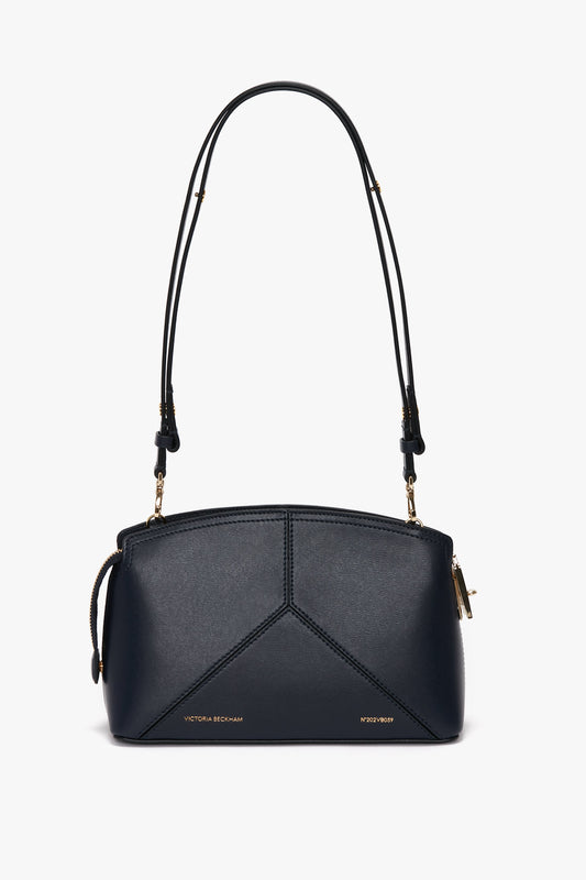 A small black leather handbag featuring two thin straps, gold hardware accents, and "Victoria Beckham" text near the bottom, enhanced with chic leather panels has been replaced by the Exclusive Victoria Crossbody Bag In Navy Leather by Victoria Beckham.