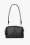 A sleek black leather handbag with a minimalist design, featuring a structured shape, gold-tone hardware, and an adjustable strap. Crafted from textured calf leather, the Victoria Crossbody Bag In Black Leather by Victoria Beckham has "Victoria Beckham" and "VB x VB 2021" embossed in gold lettering.