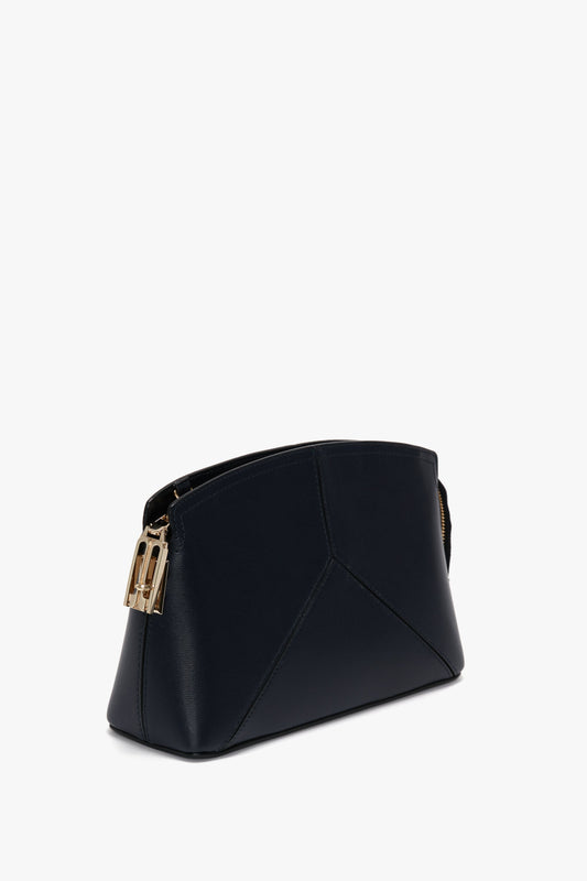 Navy, trapezoidal Exclusive Victoria Crossbody Bag In Navy Leather with a minimalist design featuring leather panels and a gold clasp detail by Victoria Beckham. Its sleek, smooth surface is set against a plain white background.
