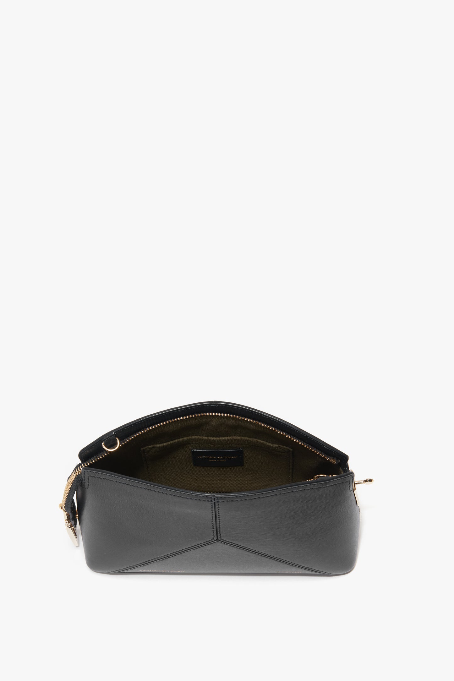 A black Victoria Beckham Victoria Crossbody Bag In Black Leather with a gold zipper is shown from above, displaying its open, empty interior lined with beige fabric.