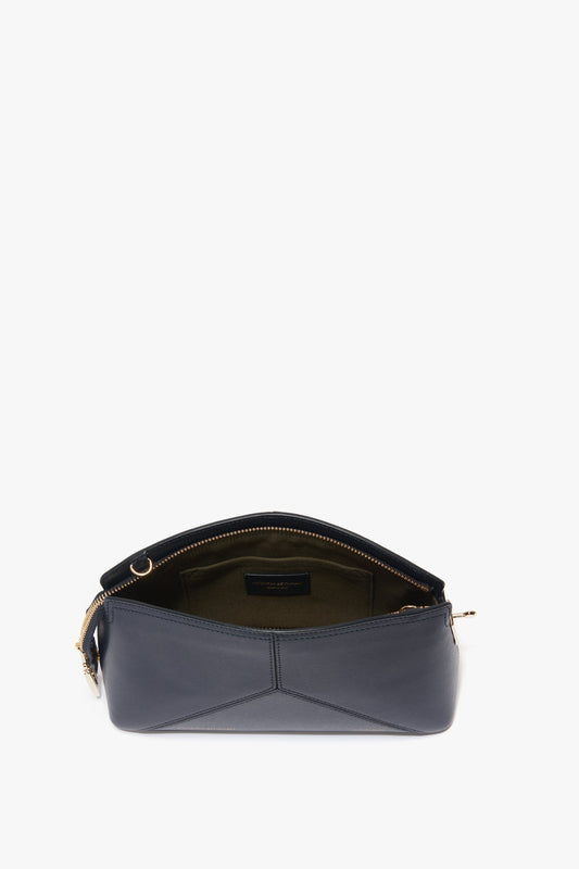 A navy **Exclusive Victoria Crossbody Bag In Navy Leather** with a partially open zipper revealing a green interior lining. The bag has gold hardware, leather panels, and a triangular pattern on the front. **Victoria Beckham**