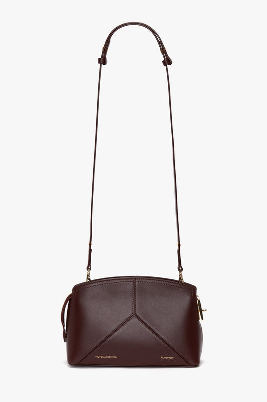 A **burgundy Victoria Crossbody Bag In Burgundy Leather** shoulder bag made of calf leather with a long adjustable strap, geometric stitching on the front, and a small gold zipper on the side from **Victoria Beckham**.