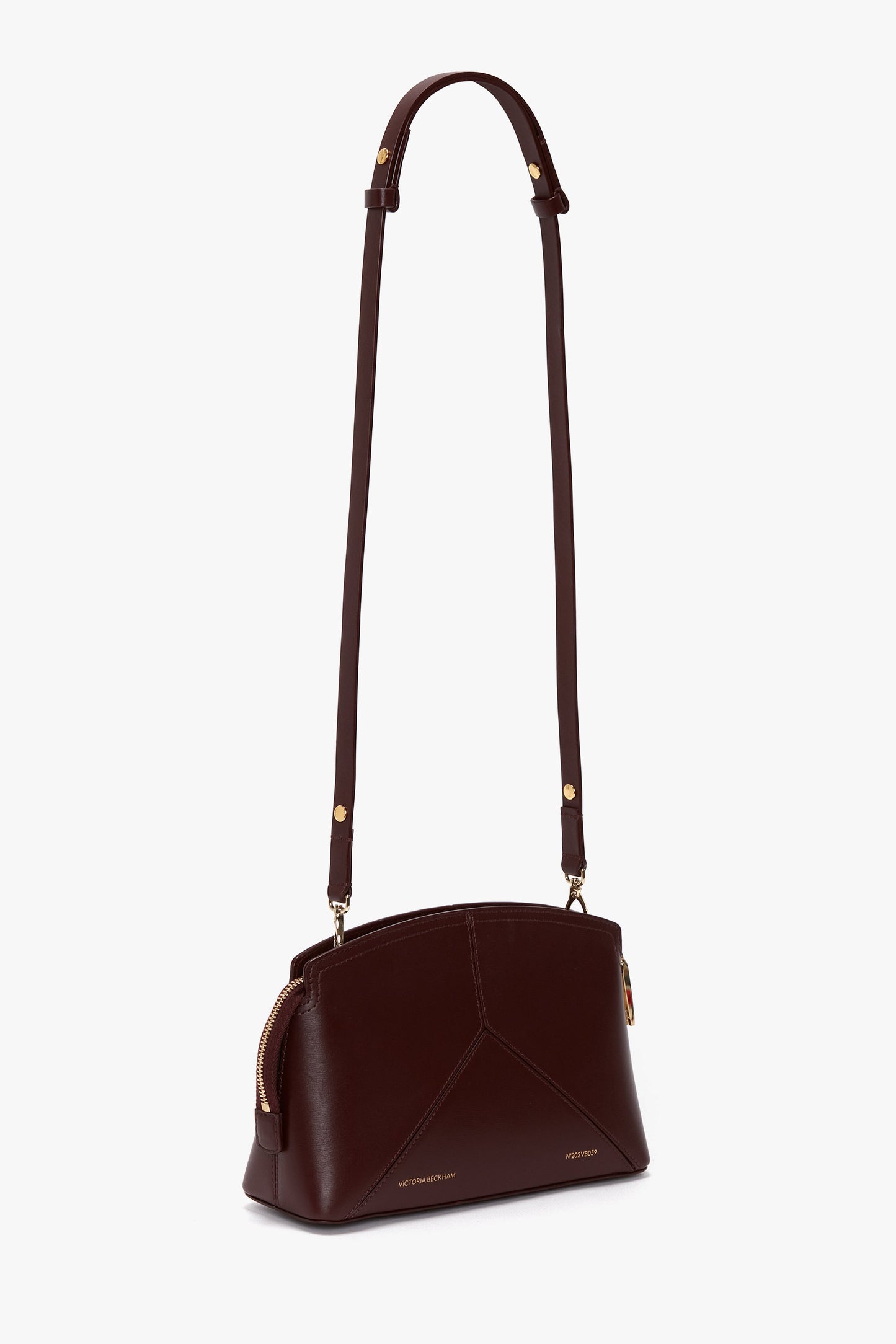 The Victoria Beckham Victoria Crossbody Bag In Burgundy Leather is a sophisticated bag crafted from rich burgundy leather, featuring an adjustable strap, gold-tone hardware, and a secure zippered top.