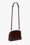 The Victoria Beckham Victoria Crossbody Bag In Burgundy Leather is a sophisticated bag crafted from rich burgundy leather, featuring an adjustable strap, gold-tone hardware, and a secure zippered top.