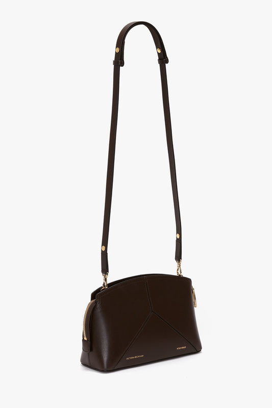 The Victoria Beckham Exclusive Victoria Crossbody Bag In Brown Leather is a dark brown calf leather bag with gold-tone hardware, an adjustable strap, and a zip closure.
