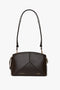 A small, brown, calf leather handbag with gold zippers and accents, featuring an adjustable shoulder strap and the name "Victoria Beckham" embossed on the front.