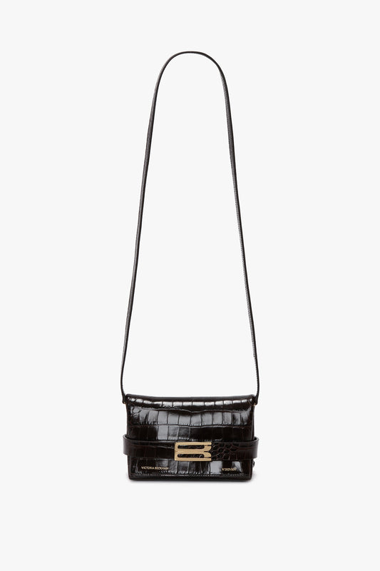 Black leather crossbody bag with crocodile texture, gold-tone clasp, and a detachable crossbody strap. Made from calf leather, this Victoria Beckham Mini B Pouch Bag In Croc Effect Espresso Leather is set against a white background.