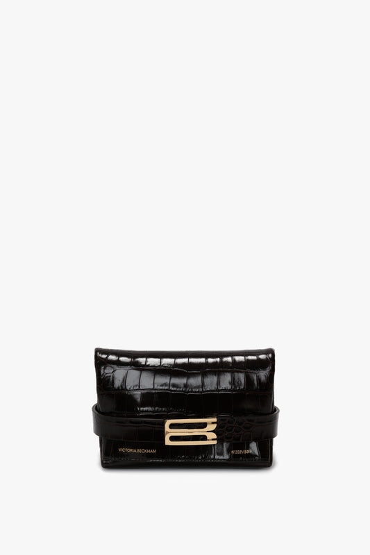 Black, crocodile-textured calf leather clutch bag with gold accents and a rectangular clasp. This Mini B Pouch Bag In Croc Effect Espresso Leather features "Victoria Beckham" embossed in gold on the lower left corner and comes with a detachable crossbody strap for versatile styling.