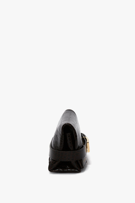 Rear view of a black, crocodile-embossed calf leather loafer with a gold buckle and a Mini B Pouch Bag In Croc Effect Espresso Leather by Victoria Beckham.