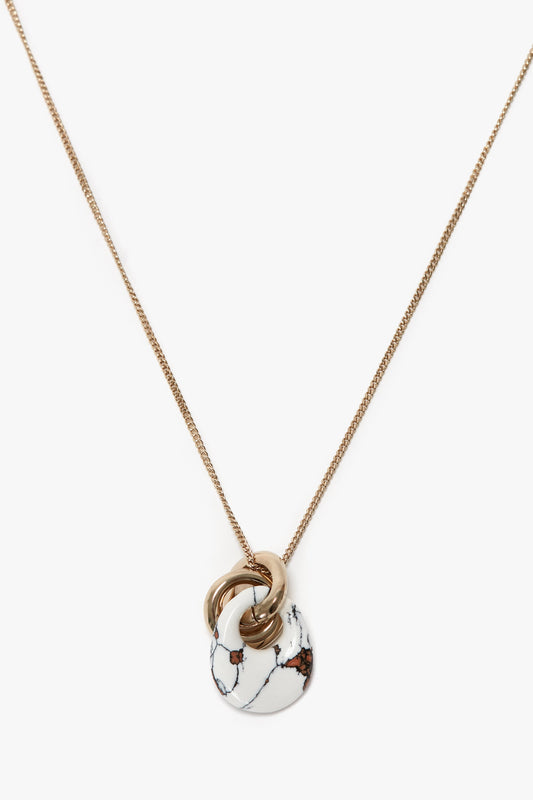 Victoria Beckham's Exclusive Resin Pendant Necklace In Light Gold-White features interlocked rings and a white circular resin pendant with a black and brown marbling effect, crafted from 100% brass.