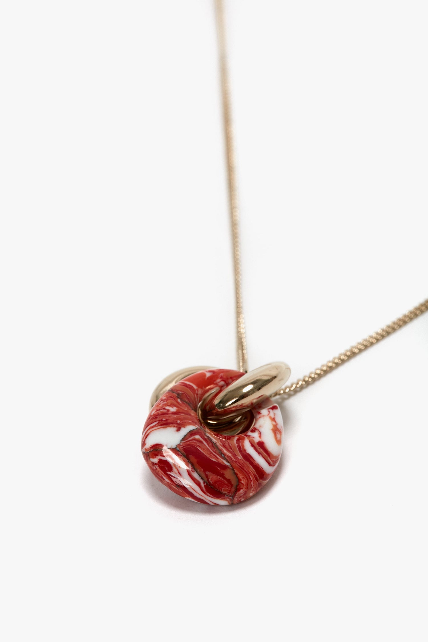 Close-up of a light gold chain necklace featuring a red and white marbled resin pendant, made in Italy. Victoria Beckham Exclusive Resin Pendant Necklace In Light Gold-Orange.