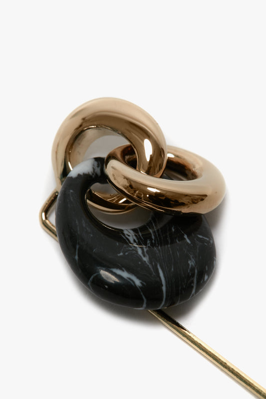 Close-up of a Light Gold/Black marbled interlocking ring hairpin on a white background, accentuated with an Exclusive Resin Charm Brooch In Light Gold-Black by Victoria Beckham.