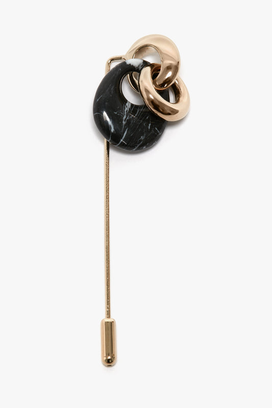 The Exclusive Resin Charm Brooch In Light Gold-Black by Victoria Beckham, adorned by two intertwined gold loops and an abstract black stone design, combines brass elements with refined artistry.