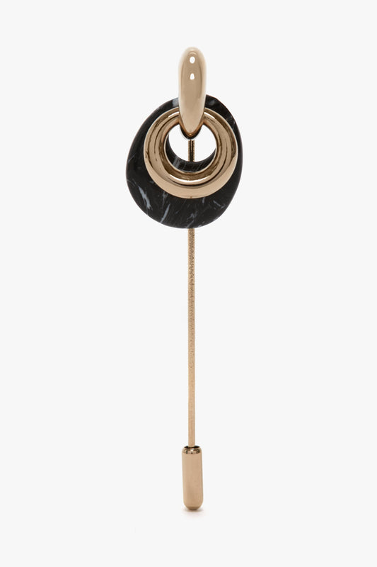 The Victoria Beckham Exclusive Resin Charm Brooch In Light Gold-Black features a metallic Light Gold/Black brass stick, a black oval element, and concentric gold rings topped with a pear-shaped gold component.