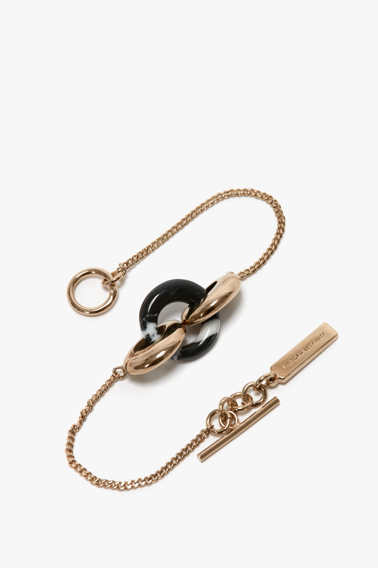 A 100% brass gold chain bracelet featuring interlocked Light Gold/Black rings at the center and a rectangular tag with engraved text near the clasp, the Exclusive Resin Charm Bracelet In Light Gold-Black by Victoria Beckham.