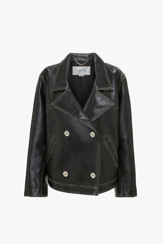 The Victoria Beckham Oversized Leather Jacket In Black, a black leather double-breasted jacket with oversized lapels and white buttons, featuring a distressed finish, is displayed on a white background.