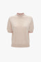 A Victoria Beckham Short Sleeve Top In Nougat with a speckled pattern, featuring a mock neck and contrasting red trim at the collar and sleeve edges, displayed on a plain white background.