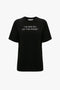 I'm Smiling On The Inside Slogan T-Shirt in Black from Victoria Beckham, featuring the text "I'M SMILING ON 'THE INSIDE'" printed in white on the front.