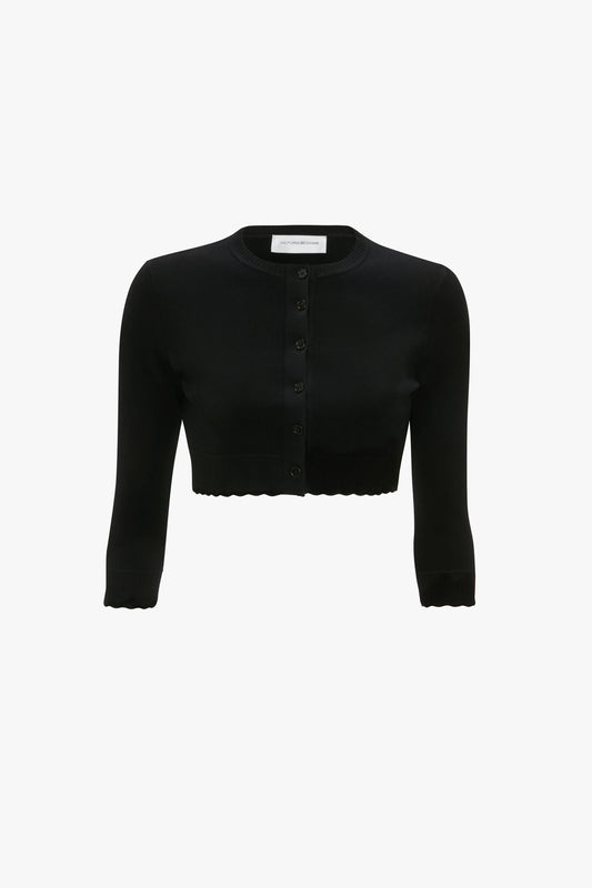 A black, long-sleeve, cropped cardigan featuring buttons down the front and scalloped hems on the sleeves and bottom edge, offering a form-fitting silhouette with feminine detailing - the VB Body Cropped Cardigan In Black by Victoria Beckham.