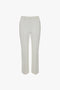 A pair of Cropped Kick Trouser In Ivory by Victoria Beckham with belt loops and a front seam detail, displayed on a white background.