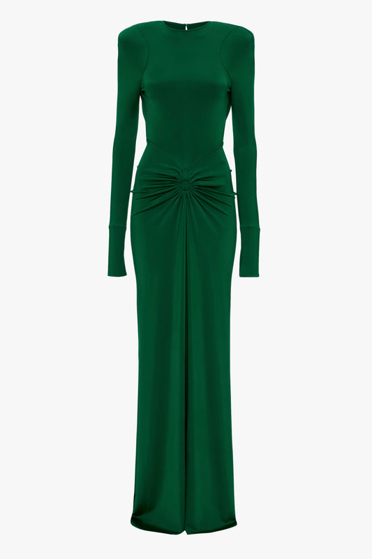 A long, green formal dress with a structured silhouette, featuring long sleeves, a high neckline, and a knotted detail at the waist is the Circle Detail Open Back Gown In Emerald by Victoria Beckham.